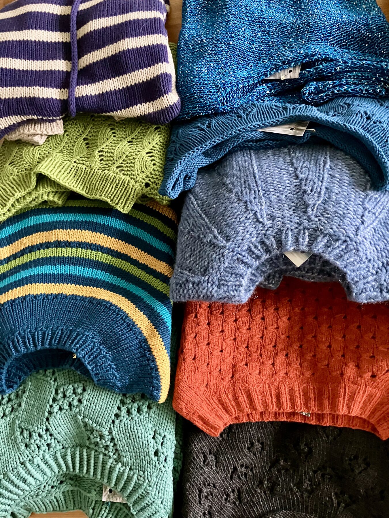 Gestapelte handgestrickte Pullover in Blau, Grün, Orange und Grau